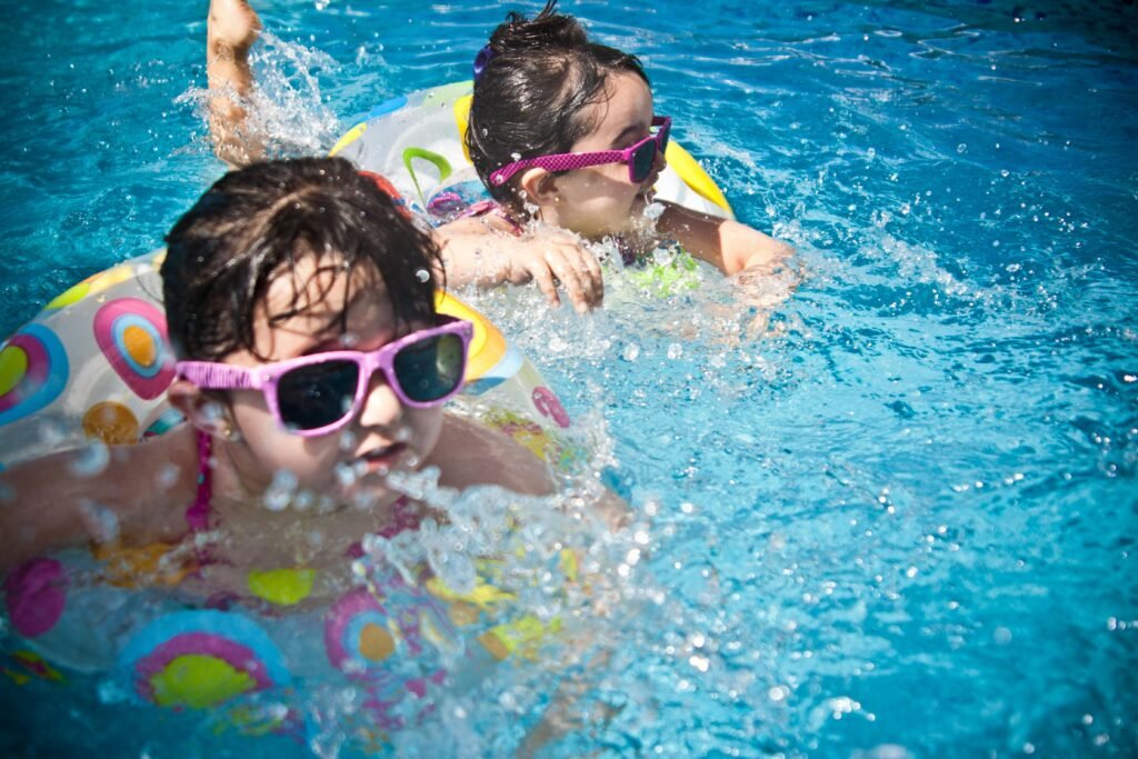 Two young girls enjoying a playful day in a bright blue swimming pool with colorful float rings.