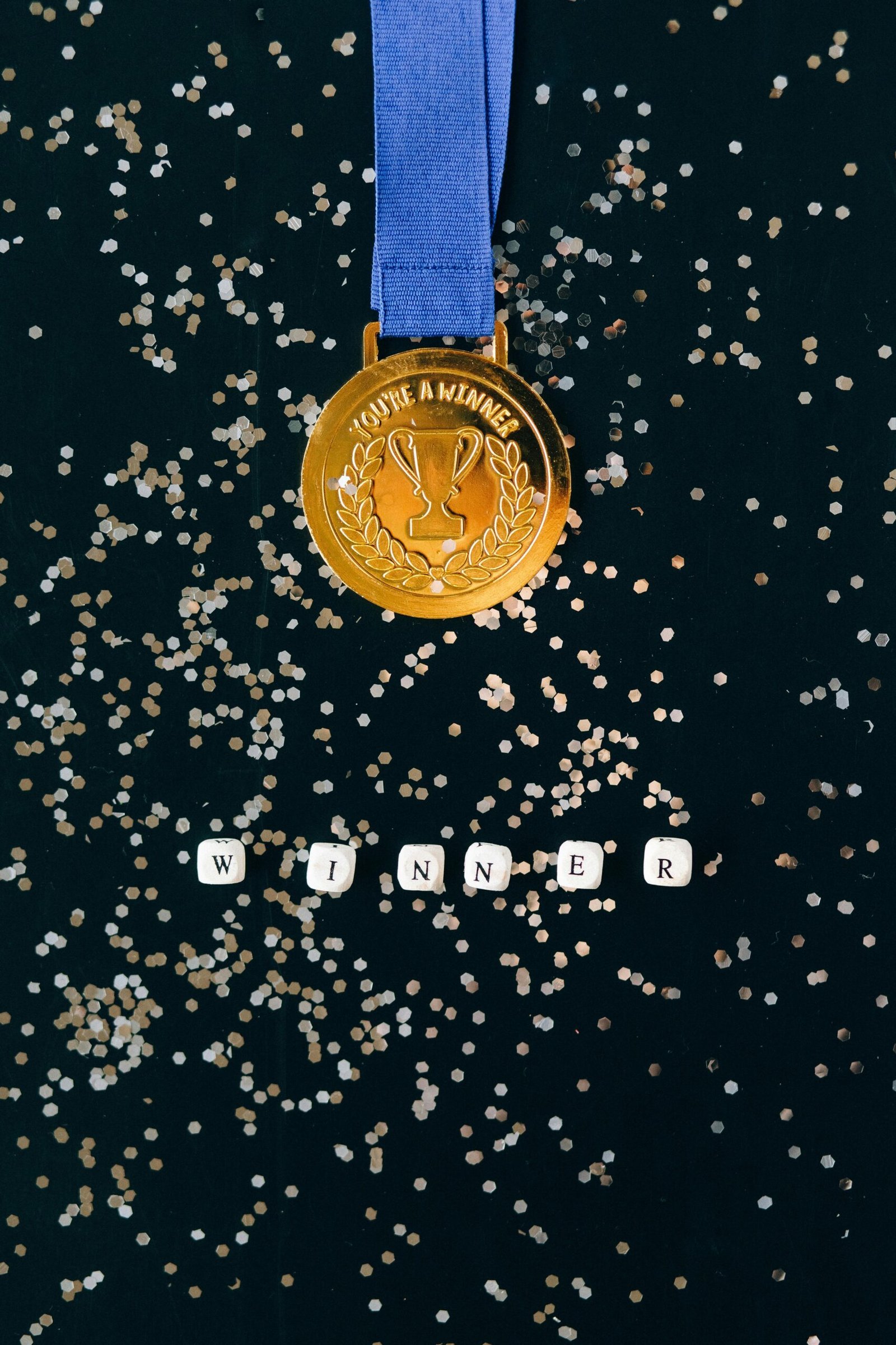 Gold medal on a black surface with confetti and 'winner' spelled out.