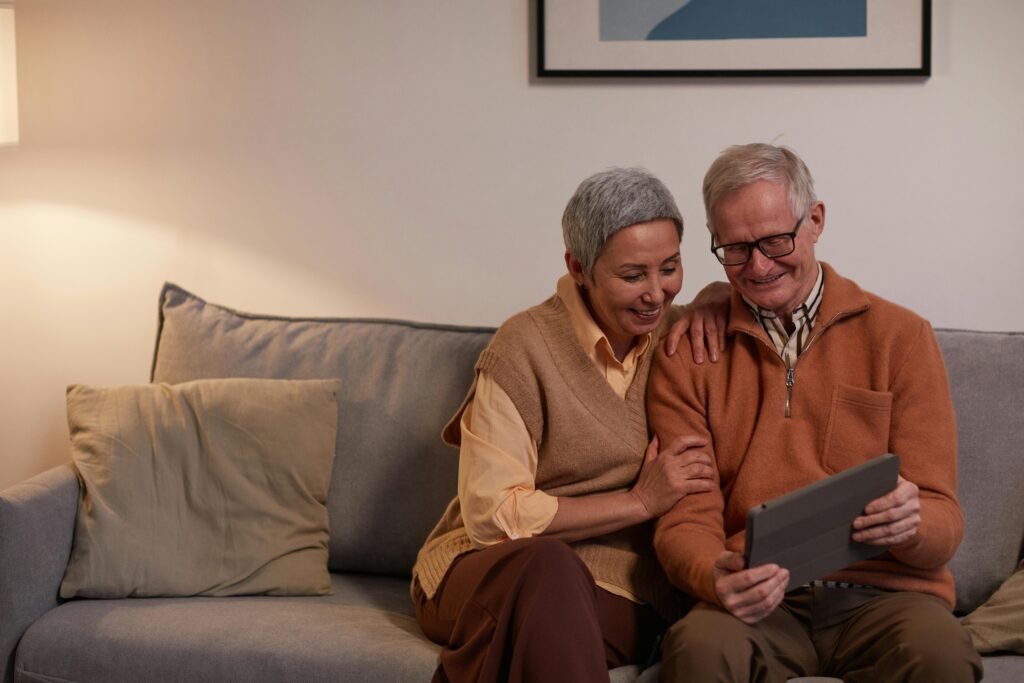 A senior couple smiling and using a tablet in their cozy living room.